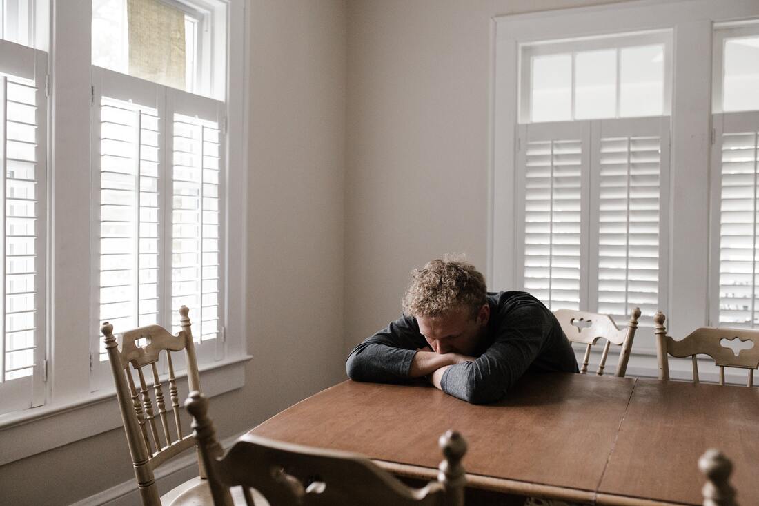 A man leans forward on a table in a depressed attitude.